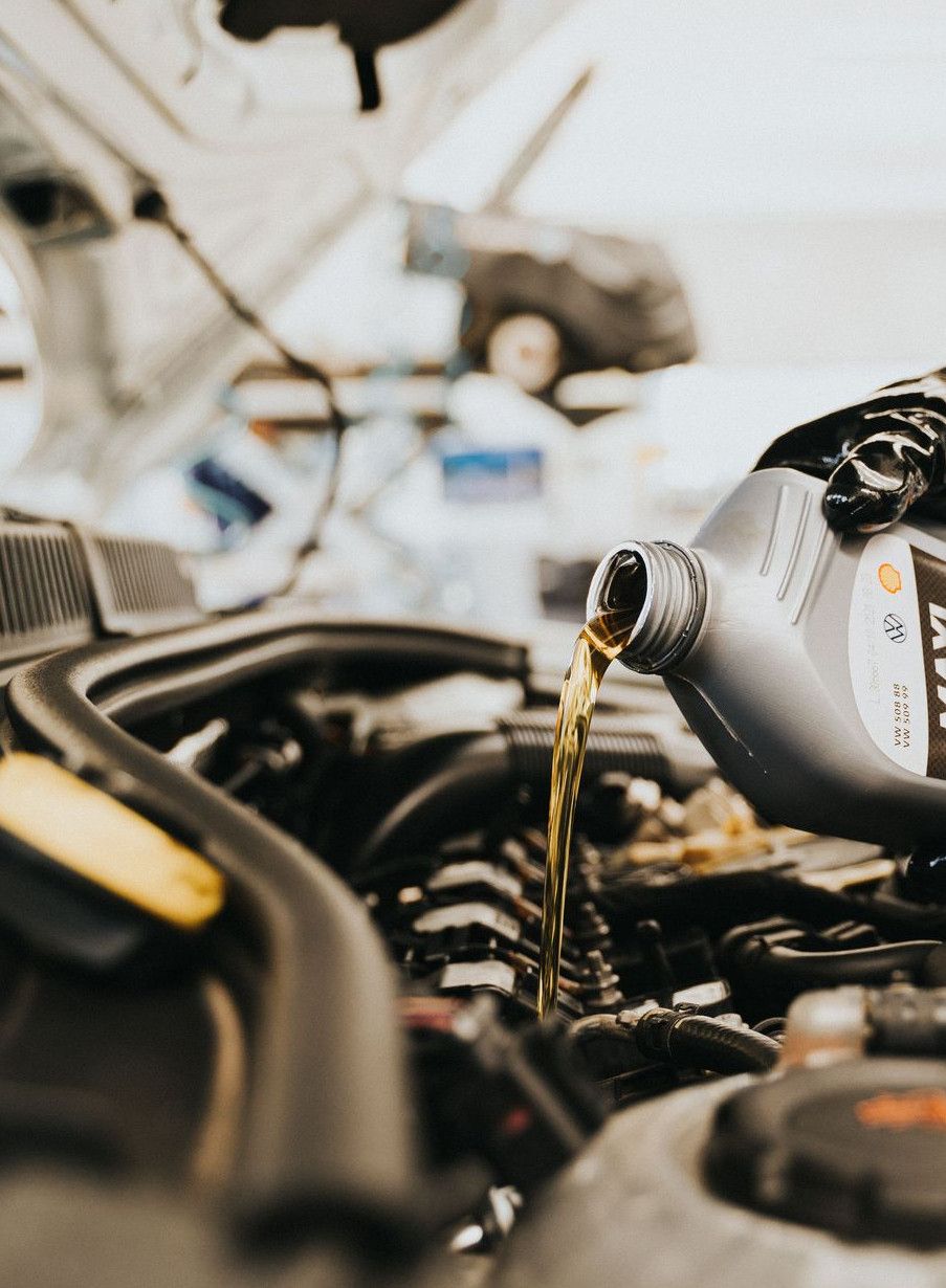 Close-up of a mechanic pouring engine oil into a car engine in an auto repair shop.