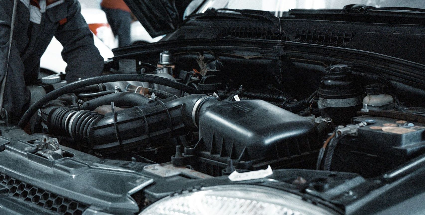 A mechanic in a grey uniform inspecting the engine of a car